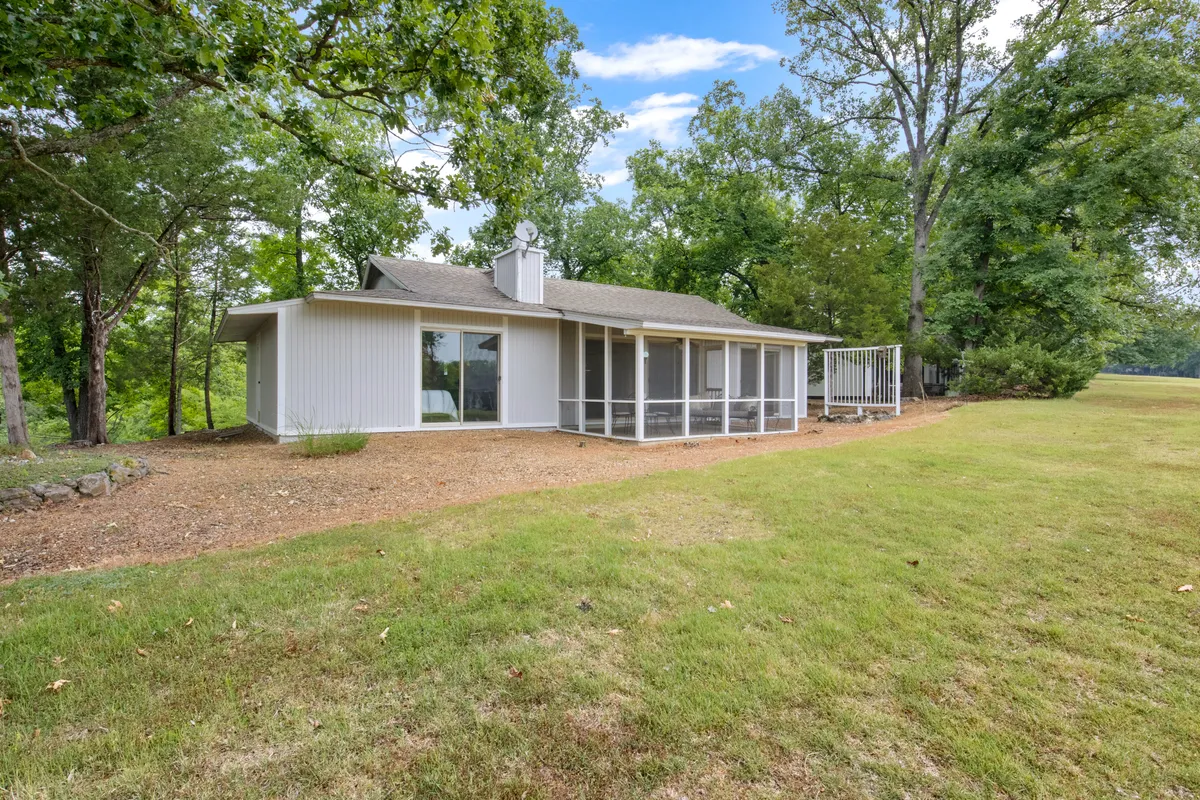 A tranquil exterior view of the house with a screened porch nestled among tall trees. The inviting porch offers a place for guests to relax and enjoy nature, while level entry and easy access underscore the home’s accessibility.