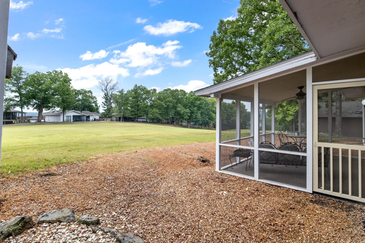 An exterior view of the screened porch opening onto an expansive lawn, framed by tall trees and lush landscaping. The spacious green area is ideal for children's play and family outdoor activities, while the porch offers a seamless transition between home and nature.