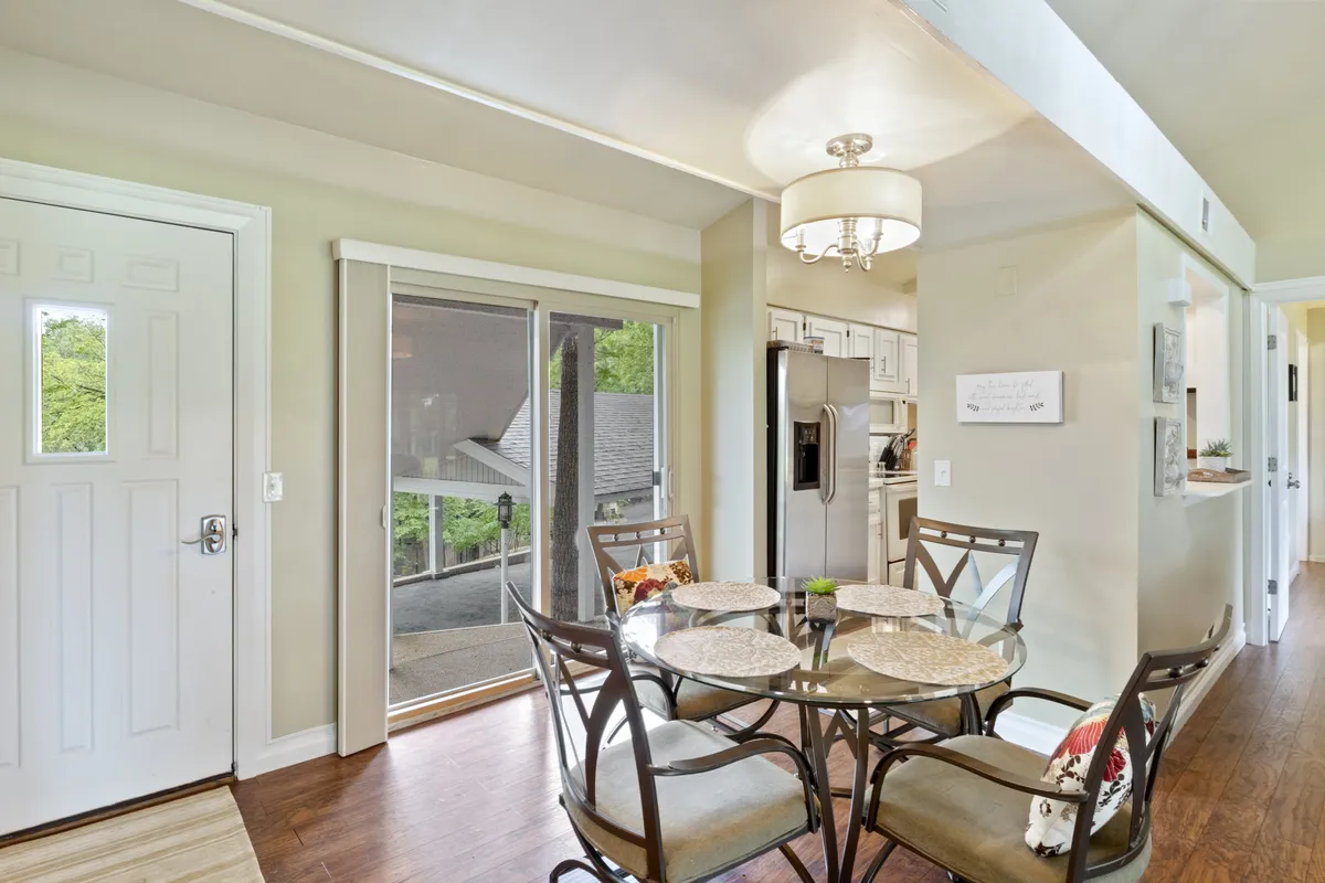 A modern dining area with a glass-topped dining table, elegant chandelier, and a sliding glass door that provides views and easy access to the outdoors. The room is bathed in natural light and arranged for group dining, meals, or board games.