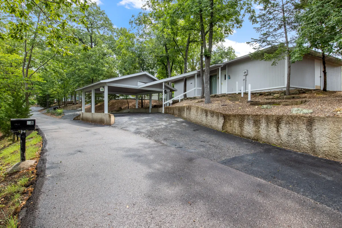 This exterior image features a peaceful driveway with a covered carport, landscaped greenery, and mature trees. The setup is welcoming and accessible, showing how arriving at the property is both easy and accommodating for guests with rolling luggage, strollers, or mobility needs.