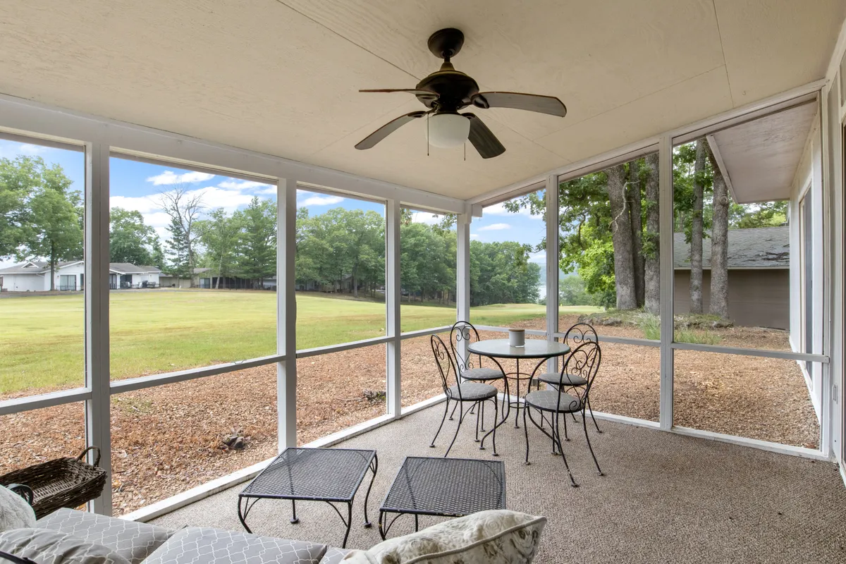 A peaceful screened-in porch featuring a table and chairs beneath a ceiling fan, with a clear view to the outdoors. Soft natural light streams in, creating an inviting setting for morning coffee, reading, or relaxed conversation while enjoying the fresh air and views of the surrounding greenery.