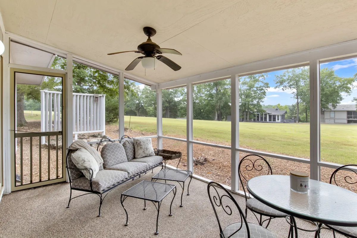 A cozy screened-in porch furnished with comfortable seating and a dining table, ideal for relaxing, entertaining, or enjoying meals with loved ones. The view through the screen highlights lush greenery and the calming effect of the outdoors.