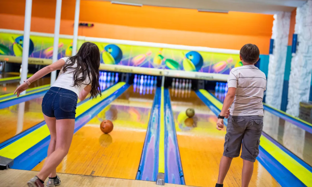 Brightly lit bowling lanes stretch into the distance, with participants engaged in playful competition. Bowling balls line the racks, and the mood is casual and fun, capturing a group activity ideal for a night out.